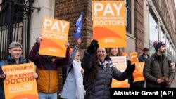 Sejumlah dokter muda membawa poster berdemo di luar Rumah Sakit St Mary di London, Inggris, 14 Maret 2023. Para perawat, paramedis, dan petugas kesehatan lainnya di Inggris sudah berdemo berbulan-bulan menuntut gaji yang layak. (Foto: Alastair Grant/AP Photo)