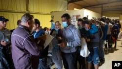 FILE - People line up for a commercial bus that will take them to the San Antonio airport at a warehouse run by the Mission: Border Hope nonprofit group run by the United Methodist Church in Eagle Pass, Texas, May 23, 2022.