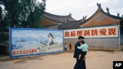 资料照 - 这张美联社的照片摄于1972年4月台湾的金门岛。一位长者抱着他的孙子走过一幅“整军经武反攻大陆“的宣传壁画。