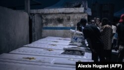 Les proches des personnes tuées fin août par l'armée à Goma, dans l'est de la RDC, regardent l'intérieur des cercueils alors qu'ils sont déchargés dans un cimetière à la périphérie de la ville, le 18 septembre 2023.