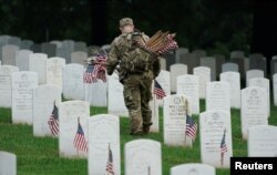 A U.S. Army Old Guard soldier places a flag at a headstone during the annual 'Flags In' event, in advance of Memorial Day at Arlington National Cemetery in Arlington, Virginia, May 23, 2024.