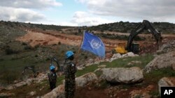 FILE - U.N. peacekeepers hold their flag as they observe Israeli excavators' attempt to destroy tunnels built by Hezbollah, near the southern Lebanese-Israeli border village of Mays al-Jabal, Lebanon, Dec. 13, 2019. 
