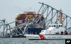 Petugas Penjaga Pantai melewati kapal kargo yang terjebak di bawah bagian struktur Jembatan Francis Scott Key di Baltimore, Maryland yang ambruk, setelah kapal kargo itu menabrak jembatan tersebut, Selasa, 26 Maret 2024. (AP/Steve Helber)