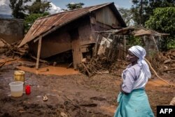 Seorang perempuan berdiri mengamati kerusakan di depan rumahnya yang hancur di daerah yang terkena dampak hujan lebat dan banjir bandang di desa Kamuchiri, dekat Mai Mahiu, 29 April 2024. (LUIS TATO / AFP)