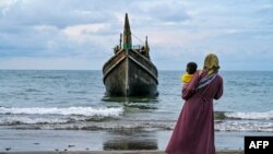 A woman with her child looks at a boat which carried Rohingya refugees to the Laweueng beach in Pidie district of Aceh province, Indonesia, Dec. 10, 2023. 