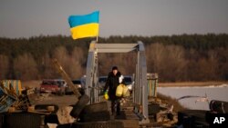 A woman crosses a makeshift pedestrian bridge connecting the two sides of a destroyed road bridge in Staryi Saltiv, Ukraine, Feb. 17, 2023.