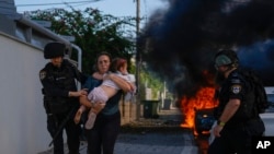 Police officers evacuate a woman and a child from a site hit by a rocket fired from the Gaza Strip, in Ashkelon, southern Israel, Oct. 7, 2023. 