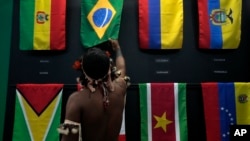 An indigenous man passes his hand over the Brazilian flag in a flag pavilion of the States parties to the Amazon Cooperation Treaty, during the Amazon Dialogue meetings at the Hangar convention center in Belem, Brazil, Aug. 6, 2023. 
