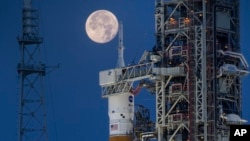 A full moon is seen behind the Artemis I Space Launch System (SLS) and Orion spacecraft, atop the mobile launcher, at NASA's Kennedy Space Center in Florida on June 14, 2022. (Cory Huston/NASA via AP)