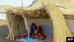 FILE - Seorang perempuan pengungsi dan anak-anaknya duduk di bawah naungan gubuk jerami di sebuah kamp di negara bagian Gadaref selatan untuk orang-orang yang melarikan diri dari negara bagian Khartoum dan Jazira di Sudan yang dilanda perang, 20 Maret 2024. (AFP)