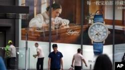 Para pengunjung melintas di depan iklan jam tangan mewah, Blancpain, dari Swiss di sebuah pusat perbelanjaan mewah di Beijing, 13 Juni 2023. (Foto: Mark Schiefelbein/AP Photo)