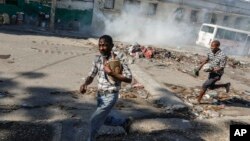 Para pria berlarian mencari perlindungan saat polisi antihuru-hara menembakkan gas air mata untuk membubarkan kerumunan di dekat Istana Nasional, di Port-au-Prince, Haiti, Selasa, 2 April 2024. (Foto: AP/Odelyn Joseph)