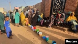 FILE - Residents wait to collect food in containers from a soup kitchen in Omdurman, Sudan, March 11, 2024. Nearly five million people in the country are close to famine as Sudan's civil war passes the one-year mark. 