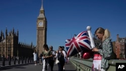 FILE - A woman holds a balloon featuring a Union Jack flag near the Houses of Parliament during a sunny day in London, Sept. 4, 2023. 