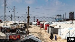 Seorang perempuan dan seorang anak kecil tampak berjalan di antara tenda-tenda di kamp al-Hol yang menampung terduga kerabat dari anggota pasukan ISIS, di Hasakeh, Suriah, pada 3 Maret 2021. (Foto: AFP/Delil Souleiman)