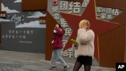 两个年轻人走过北京街头一堵政府的宣传墙。（2024年1月17日）