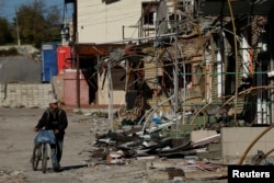 FILE - A man walks with his bicycle through a shopping street destroyed by Russian strikes in the town of Kupiansk, Ukraine, Oct. 18, 2022.