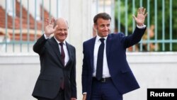 Kanselir Jerman Olaf Scholz dan Presiden Prancis Emmanuel Macron mekambaikan tangan saat bertemu di Istana Meseberg, di utara Berlin, Jerman, pada 28 Mei 2024. (Foto: Reuters/Liesa Johanssen)