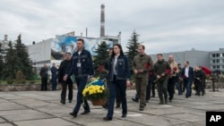 Chernobyl nuclear power plant workers carry flowers to the monument honoring victims of the 1986 explosion and fire at the plant in Chernobyl, Ukraine, April 26, 2023.