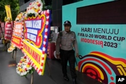 Seorang satpam berjalan di antara spanduk FIFA U-20 World Cup dan karangan bunga belasungkawa yang dikirim oleh suporter sepak bola, di luar gedung kantor Persatuan Sepak Bola Seluruh Indonesia, PSSI, di Jakarta, 30 Maret 2023. (AP/Dita Alangkara)