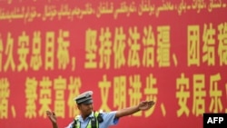 Seorang polisi tampak berdiri di depan papan iklan propaganda yang berbunyi "pemeliharaan aturan hukum di Xinjiang" yang ditulis dalam Bahasa Mandarin dan Uyghur dan terpasang di sebuah jalan di prefektur Kashgar, Xinjiang, pada 19 Juli 2023. (Foto: AFP/Pedro Pardo)