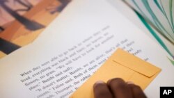 Michael Crowder, 11, follows along with a bookmark as he reads during an after-school literacy program in Atlanta, April 6, 2023. When he's not in school, Michael has been dropping by his apartment complex’s community center most afternoons to read books to the staff, who encourage the activity with pizza parties. His report cards show improvement. His parents have noticed his growth.
