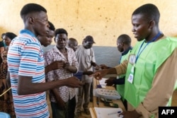 Men show their ID's to polling station officials to vote in the school polling station in the Abena district, Bureau 2 Carré 27, in N'Djamena on May 6, 2024.