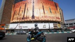 তেহরানে ইরানি ক্ষেপণাস্ত্রের ছবি সম্বলিত একটি বিলবোর্ডের পাশ দিয়ে এক ব্যক্তি মোটরসাইকেল চালিয়ে যাচ্ছেন। ১৯ এপ্রিল, ২০২৪।