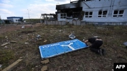 This photo taken Aug. 16, 2024, during a media tour organized by Ukraine, shows a man examining a damaged road sign with arrows to Ukraine and Russia, at a destroyed border crossing near the Ukraine-held town of Sudzha, in Russia's Kursk region.
