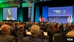 台湾海军司令唐华上将(第二排左2）与台湾驻美军事代表团团长魏中兴(第二排左1)参加美国海军联谊会“海空天”2024年会。屏幕上为美国海军作战部部长丽莎弗朗切蒂上将。(2024年4月8日，美国之音锺辰芳拍摄)