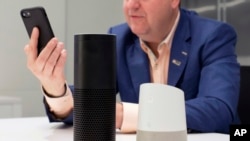 FILE - A man holds an iPhone next to an Amazon Echo, center, and a Google Home, right, in New York, June 14, 2018. 