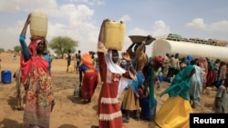 FILE - Sudanese refugee women who fled violence in Sudan's Darfur region, carry jerrycans of water as they walk to their shelter near the border between Sudan and Chad in Koufroun, Chad, May 10, 2023.