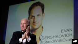 President Joe Biden stands with the audience and applauds as an image of journalist Evan Gershkovich appears onscreen during the White House Correspondents' Association dinner at the Washington Hilton in Washington,, Apr. 29, 2023. 