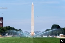 Sprinklers water the National Mall on by a sign announcing the Smithsonian Folklife Festival at the National Mall in Washington, June 26, 2024.
