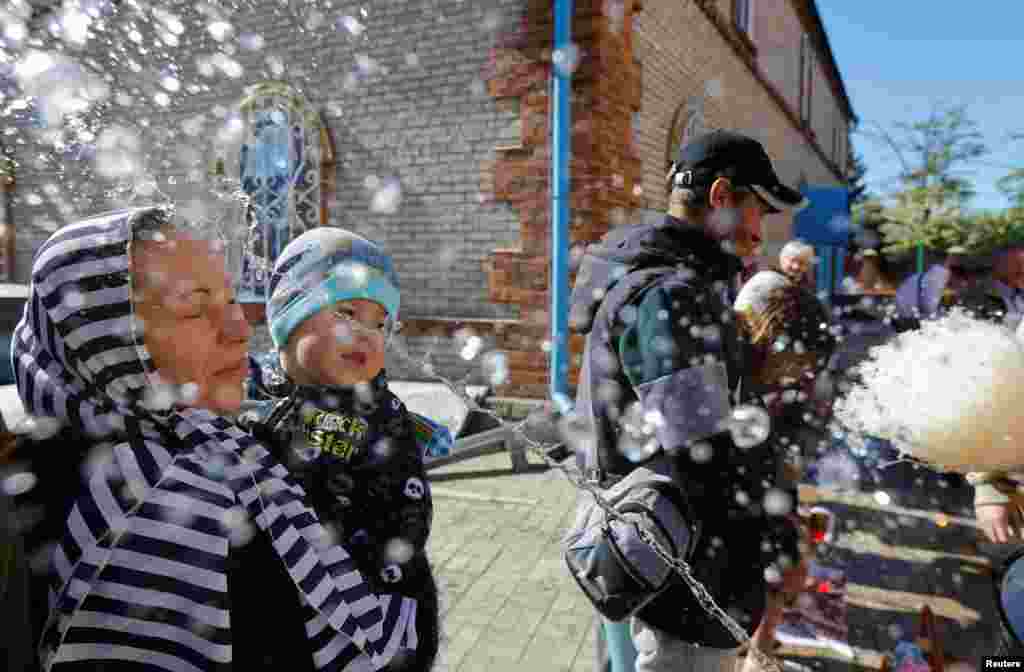 A priest sprinkles holy water on believers during Orthodox Easter celebrations near St. Nicholas Cathedral in the course of Russia-Ukraine conflict in Mariupol, Russian-controlled Ukraine, May 5, 2024. 