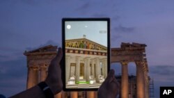 FILE - A man holds up a tablet showing a digitally overlaid virtual reconstruction of the ancient Parthenon temple, at the Acropolis Hill in Athens, Greece, June 13, 2023. 