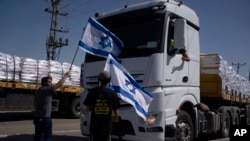 People holding Israeli flags stand in front of trucks carrying humanitarian aid as they try to stop them to enter in the Gaza Strip in an area near the Kerem Shalom border crossing between Israel and Gaza, in southern Israel, May 9, 2024.