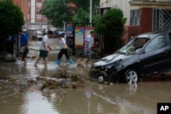 Residents walk past a vehicle damaged and left stranded by flood waters in the Mentougou district on the outskirts of Beijing, China, Aug. 1, 2023.