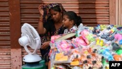 People sit in front of a table fan to cool off on a hot summer afternoon in Varanasi, India, May 29, 2024.
