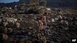 FILE - Jaquelin Stocklein of Germany drops water to a burnt area during a wildfire near the seaside resort of Lindos, on the Aegean Sea island of Rhodes, southeastern Greece, on July 24, 2023.