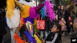 A child swings at a pinata during a street "posada" organized by neighbors in Mexico City, Dec. 22, 2023. 
