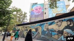 People walk past a billboard showing a portrait of newly appointed Hamas leader Yahya Sinwar (top) next to Palestine Square in the Tehran, Aug. 12, 2024. 