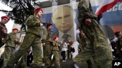 FILE - Youths help mark the ninth anniversary of the Crimea annexation from Ukraine with the banner reading "Russia doesn't start wars, it ends them," next to an image of Russian President Vladimir Putin in Yalta, Crimea, March 17, 2023.