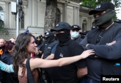 ახალგაზრდა დემონსტრანტი და ნიღბიანი პოლიციელები