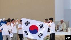 Young pilgrims from South Korea celebrate with their national flag and with Pope Francis after he announced that the next World Youth Day, will be in Seoul, South Korea in 2027, at the end of a mass at Parque Tejo in Lisbon, Aug. 6, 2023. 