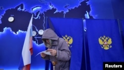 A woman studies her ballot during the presidential election in Novosibirsk, Russia, March 15, 2024. 