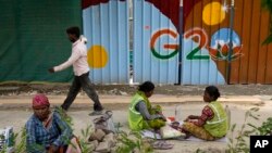 Laborers take a lunch break near a construction site covered with G20 summit logo in New Delhi, India, Thursday, Aug. 24, 2023. (AP Photo/Manish Swarup)