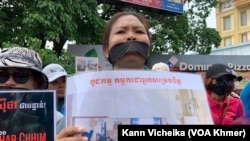 ក្រុមបុគ្គលិក និងសហជីពណាហ្គាវើលដ៍ ឈរលើកបដា និងរូបថត គាំទ្រថ្នាក់ដឹកនាំសហជីពរបស់ខ្លួន នៅខឿនផ្លូវម្ខាងទៀតពីមុខតុលាការ នៅថ្ងៃទី២៥ ខែឧសភា ឆ្នាំ២០២៣។ (កាន់ វិច្ឆិកា/វីអូអេ)