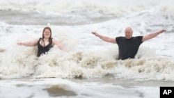 Jeremy Reddout and his daughter, Elexus, enjoy the waves between Murdoch's and Pleasure Pier as rain falls in Galveston, Texas, June 19, 2024.
