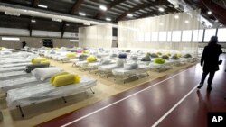 FILE - A passer-by walks through a portion of the Cass Recreational Complex, in Boston, Jan. 31, 2024, that has been turned into a temporary shelter site for families experiencing homelessness.